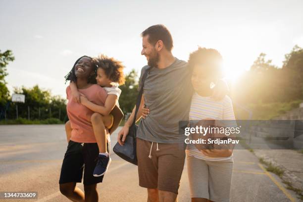 famiglia gioiosa mista, divertendosi mentre lascia il campo sportivo dopo aver finito con una partita di basket - carrying sports bag foto e immagini stock