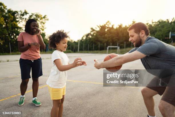 healthy and active multiracial family, father and daughter having so much fun while she shooting in the imagined hoop her father makes with a hands, while mother cheering her - 繼父 �個照片及圖片檔