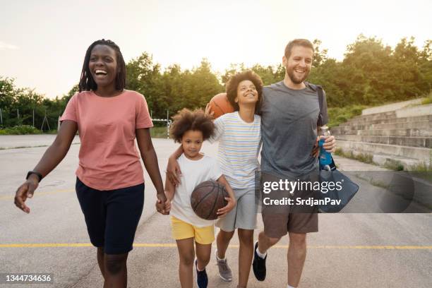 cheerful blended family, leaving the sports court while holding hands - mixed race person stockfoto's en -beelden