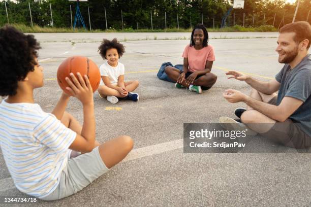 famiglia gioiosa e giocosa mescolata, passando la palla in giro mentre si è seduti in cerchio - bambini seduti in cerchio foto e immagini stock