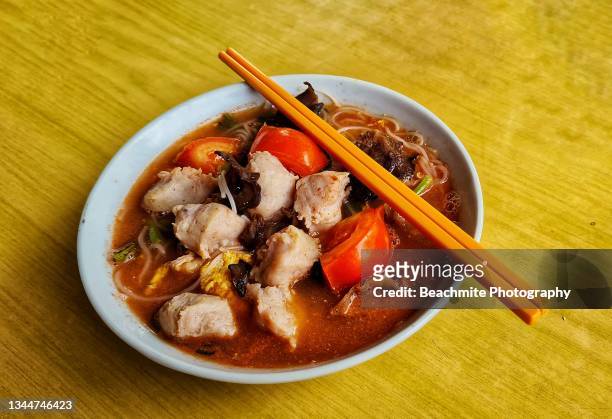 high angle view of rice noodle in red broth with fishballs and seasonal vegetables in a bowl with chopsticks on the side - broth stock pictures, royalty-free photos & images