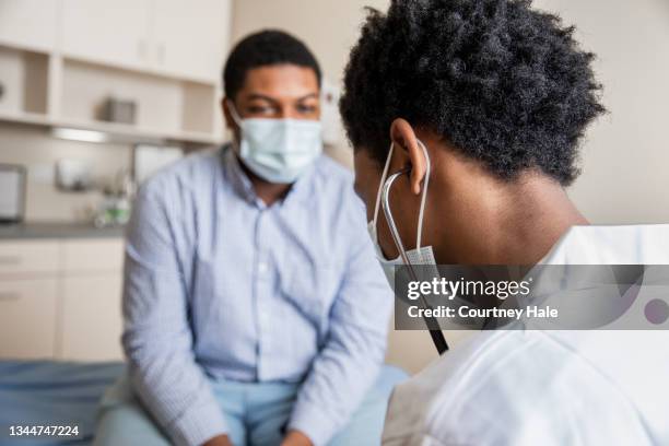 homme assis sur une table d’examen dans le bureau du médecin pendant que le médecin prend des notes - table dexamen médical photos et images de collection