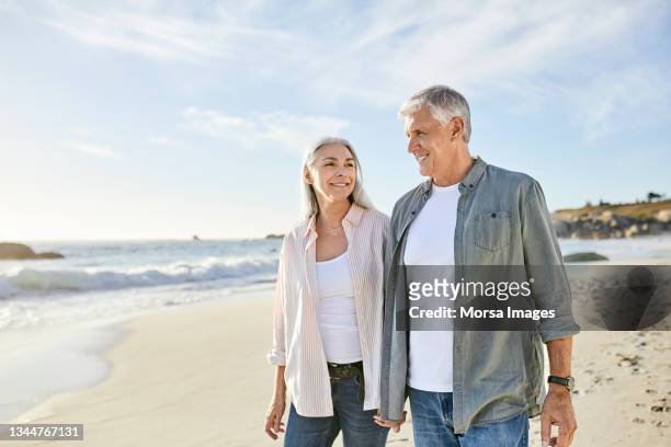 mature couple walking at beach during vacation - mature couple stockfoto's en -beelden