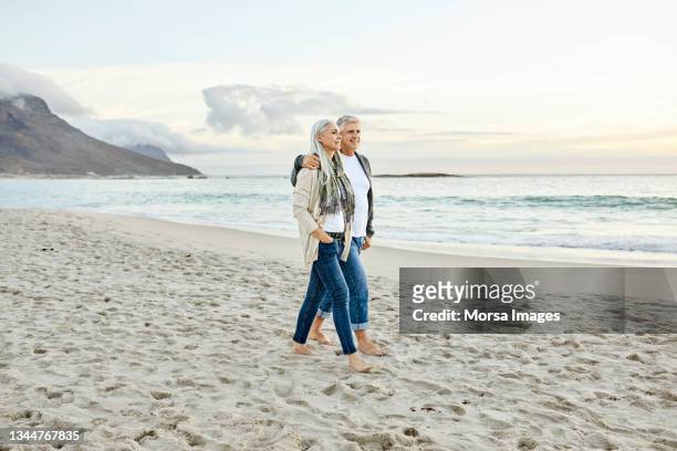 coppia che cammina in spiaggia durante il tramonto - couple walking on beach foto e immagini stock