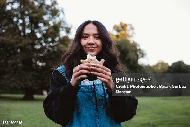 a beautiful young woman eating a sandwich in a public park. - young woman healthy eating stockfoto's en -beelden