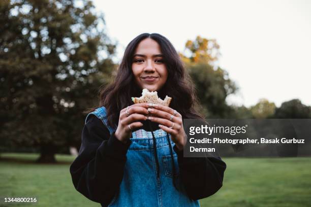 a beautiful young woman eating a sandwich in a public park. - lanche imagens e fotografias de stock