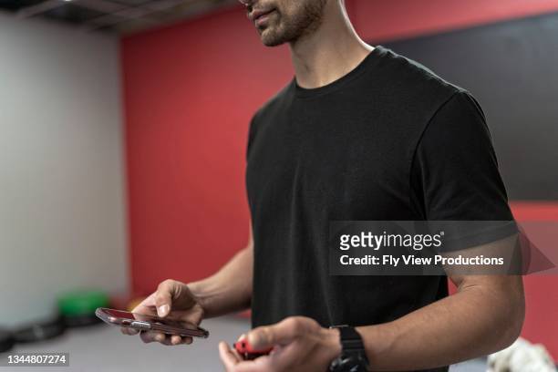 cropped shot of personal trainer using smart phone between coaching sessions - boutique gym stock pictures, royalty-free photos & images