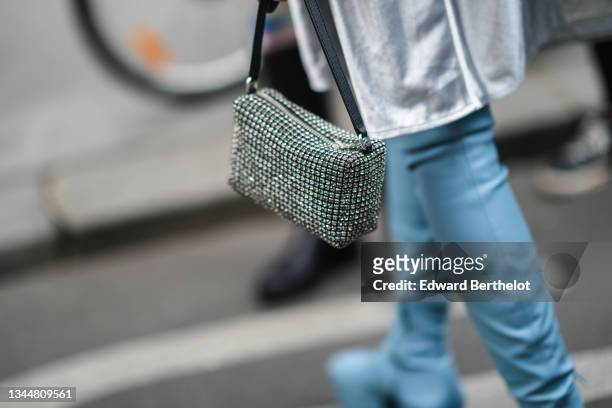 Alexandra Guerain wears a white with cut-out mesh yoke oversized long shirt with shiny silver back, a black with embroidered rhinestones handbag,...