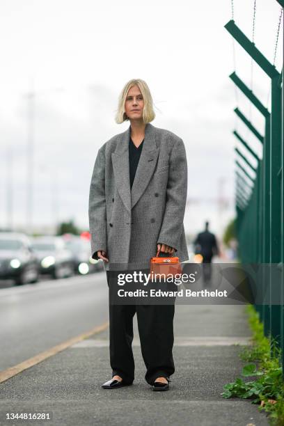 Linda Tol wears a black V-neck wool pullover, a black and gray braided wool oversized pullover, a gold ring, an orange shiny leather Kelly handbag...