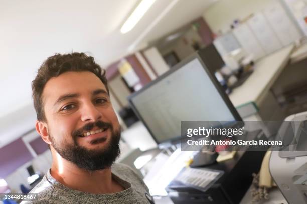 bearded man in office smiles looking at camera - selfie stock pictures, royalty-free photos & images