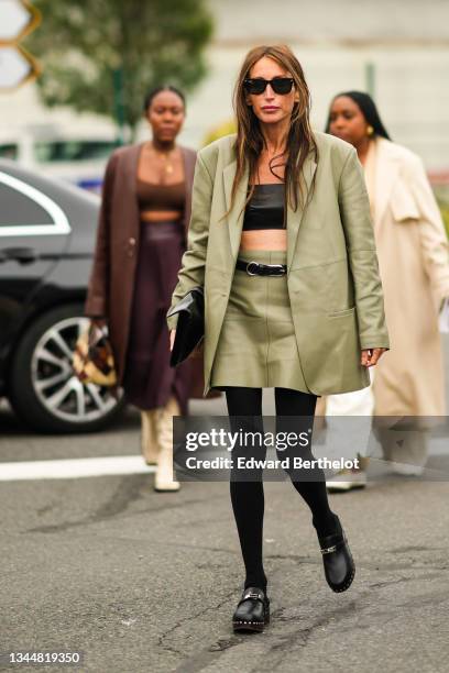 Chloe Harrouche wears sunglasses, a black leather shoulder-off / cropped top, a khaki shiny leather oversized blazer jacket, a matching khaki shiny...