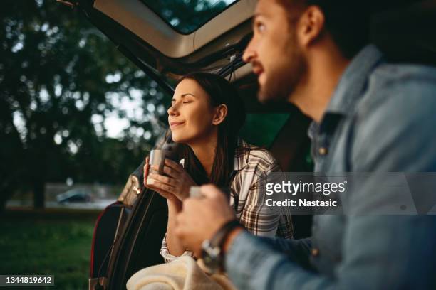 young couple in love sitting in car drinking coffee during sunset - couple in car stock pictures, royalty-free photos & images