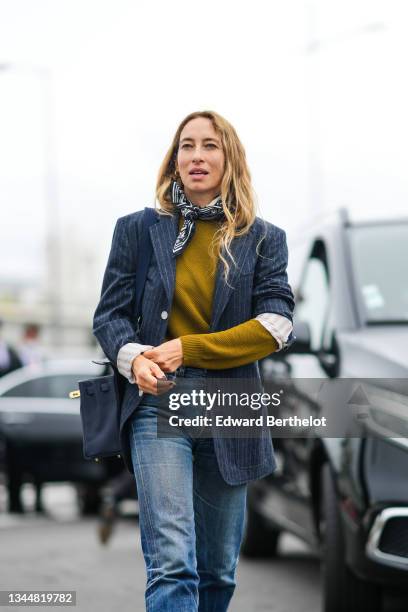 Alexandra Golovanoff wears gold earrings, a black and white print pattern silk scarf, a yellow mustard braided wool pullover, a navy blue with white...