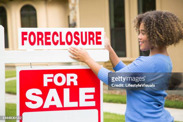 lovely young adult real estate agent standing beside her for sale sign in front yard of home.  she holds a portfolio and wears a blue top and jeans. - pantövertagande bildbanksfoton och bilder