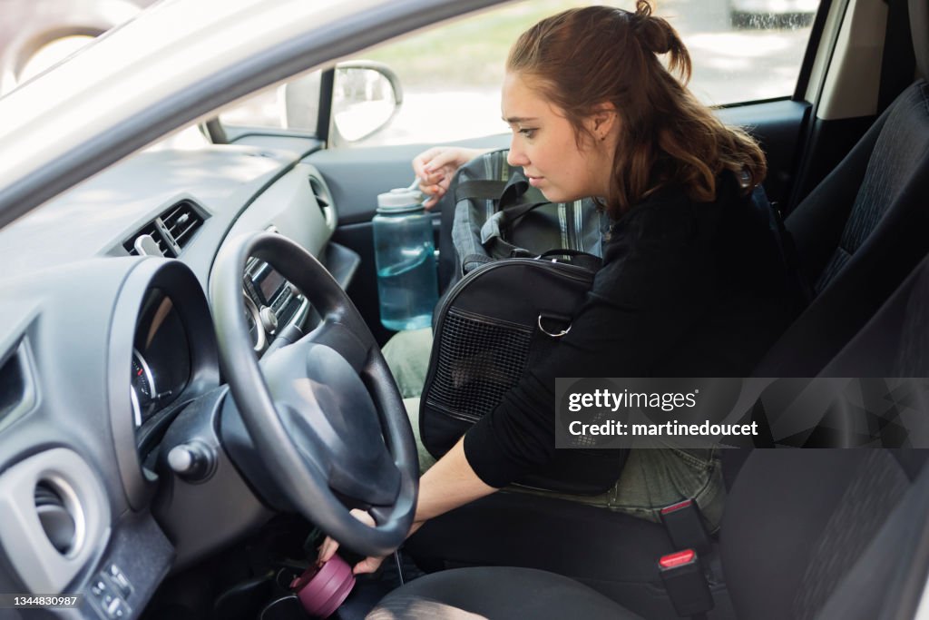 Millennial woman and newly adopted kitten in pet carrier in car.