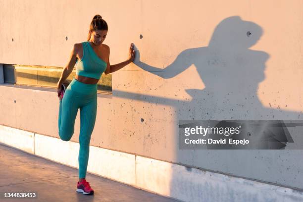 fit woman stretching legs near wall - legging stockfoto's en -beelden