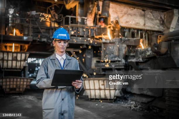 attractive caucasian woman making notes on digital tablet in factory workshop - molten stock pictures, royalty-free photos & images
