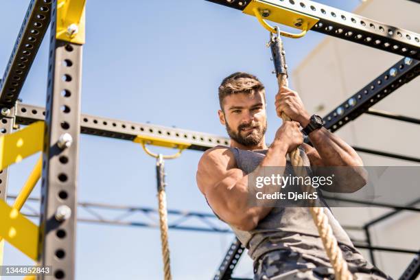 young bodybuilder climbing a rope for a strength exercise. - resistência imagens e fotografias de stock