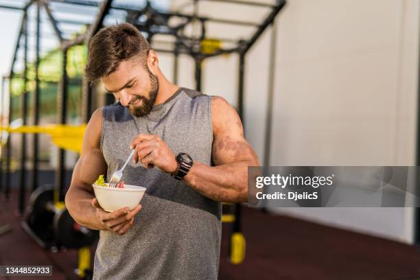 feliz joven culturista comiendo una ensalada de verduras. - bodybuilder fotografías e imágenes de stock