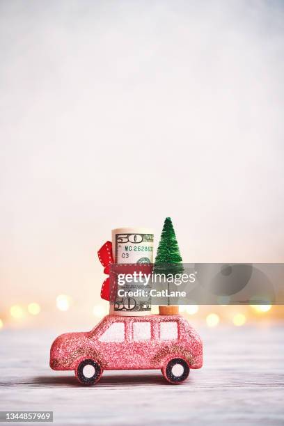 pink glittery car carrying american dollars and christmas tree with christmas lights in background - christmas toys wooden background stockfoto's en -beelden