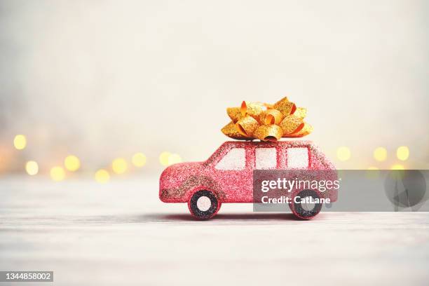 cute glittery pink car with gold bow on roof and christmas lights in background - christmas toys wooden background stockfoto's en -beelden