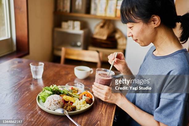 japanese woman eating a vegan lunch at a vegan cafe - only mature women stock pictures, royalty-free photos & images