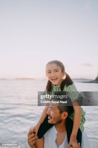 father carrying young daughter on shoulders on beach at sunset, japan - carrying on shoulders stock pictures, royalty-free photos & images