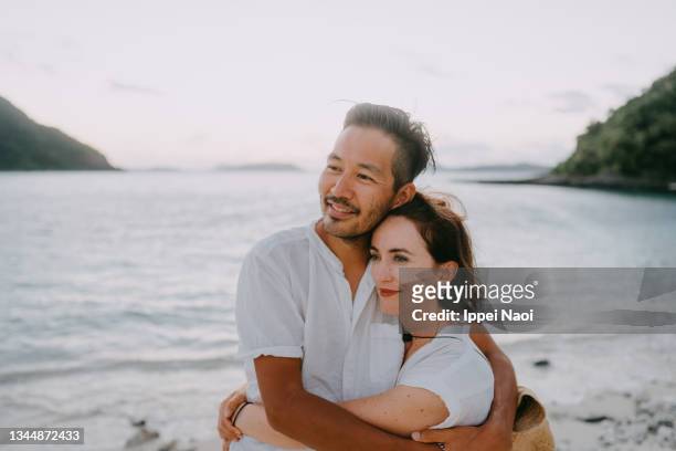 couple embracing on beach at sunset, okinawa, japan - japan beach stockfoto's en -beelden