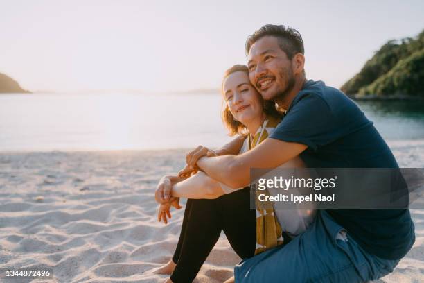 husband embracing wife from behind on beach at sunset, japan - japanese couple beach stock-fotos und bilder