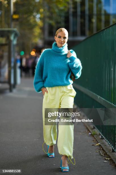 Leonie Hanne wears a gold and silver large pendant earrings, a blue fluffy turtleneck oversized pullover, a brown shiny leather with a chain shoulder...