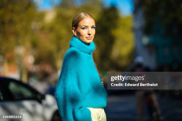 Leonie Hanne wears a gold and silver large pendant earrings, a blue fluffy turtleneck oversized pullover, pale yellow high waist cargo pants, outside...