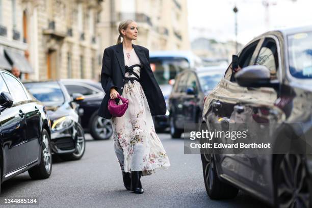 Leonie Hanne wears silver earrings, a white silk with red / purple / green / yellow fruit print patterns long ruffled / flowing dress with two black...