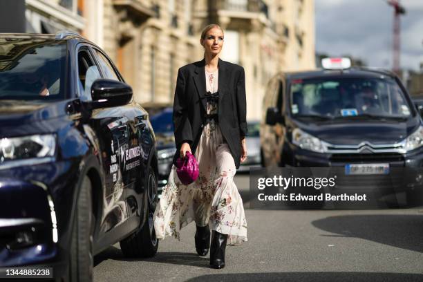 Leonie Hanne wears silver earrings, a white silk with red / purple / green / yellow fruit print patterns long ruffled / flowing dress with two black...