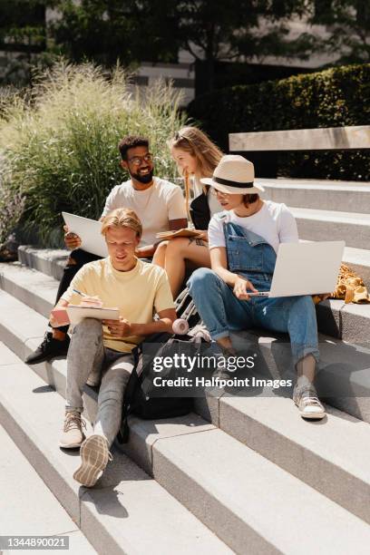 young university students with laptop sitting outdoors on stairs, talking. back to university concept - gruppo di studenti campus foto e immagini stock