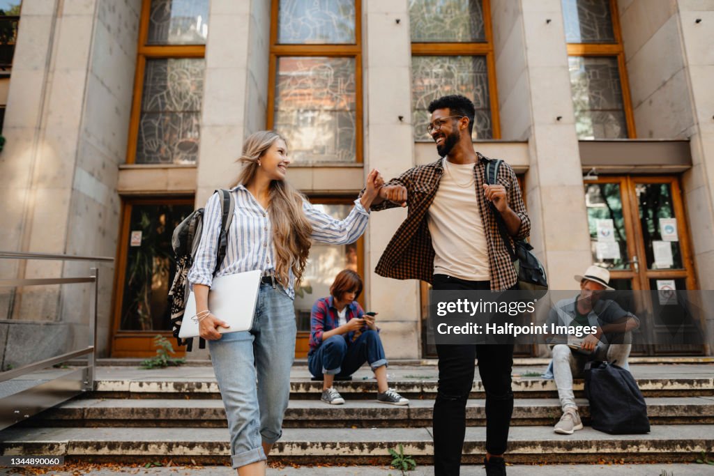 Low angle view of happy young university students greeting outdoors in front of campus. Back to university concept.