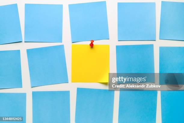 yellow sticky sticker on a white background for reminding information, attached with a paper clip. a piece of paper. space for text. there are empty blue stickers next to it. - reminder on pinboard stock pictures, royalty-free photos & images