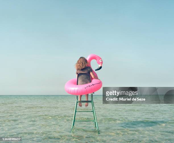 young woman with flamingo, sitting in sea, on tennis chair. - flamingos stock-fotos und bilder