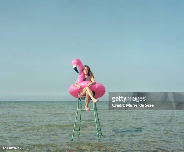 young woman with flamingo, sitting in sea, on tennis chair. - flamingos stock-fotos und bilder