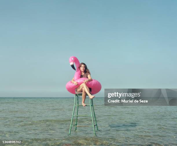 young woman with flamingo, sitting in sea, on tennis chair. - plastic flamingo stock pictures, royalty-free photos & images