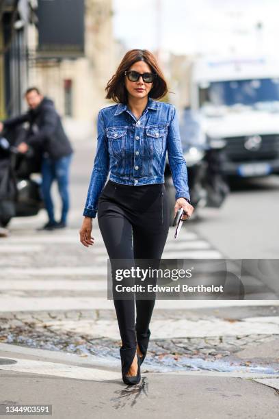 Christine Centenera wears black sunglasses, a blue denim cropped jacket, black high waist slit / split legging pants, black suede pointe pumps heels...