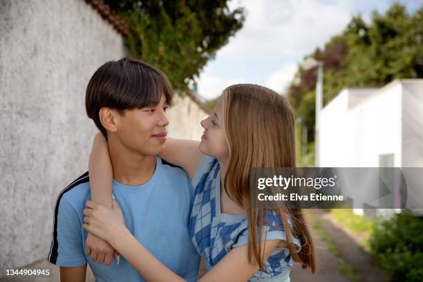 happy teenage girl and boy outdoors in summertime standing in an urban alleyway, looking at each other and smiling. - tcs stock pictures, royalty-free photos & images