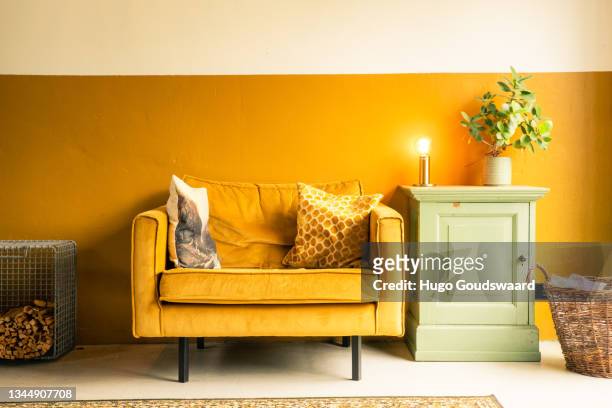 interior of a house. mustard yellow velvet loveseat. living room with midcentury modern furniture. concrete floor. vintage carpet. eclectic living room. - yellow sofa stock pictures, royalty-free photos & images