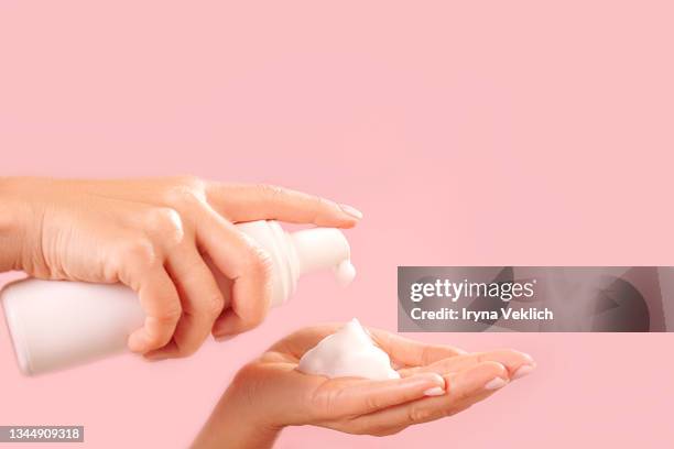 beautiful female hands with soap or cosmetic milk or washing foam on trendy pink color background. - soap dispenser stock pictures, royalty-free photos & images