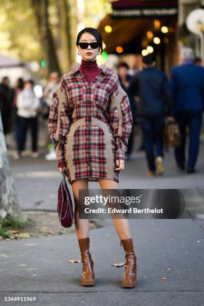 Meng Mao wears black sunglasses, silver earrings, a red shiny sequins turtleneck t-shirt, a beige and burgundy checkered pattern with beige ribbed...