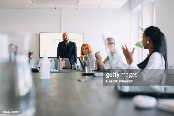 businesswoman sharing ideas with male and female colleagues in board room post covid-19 - board room stock pictures, royalty-free photos & images