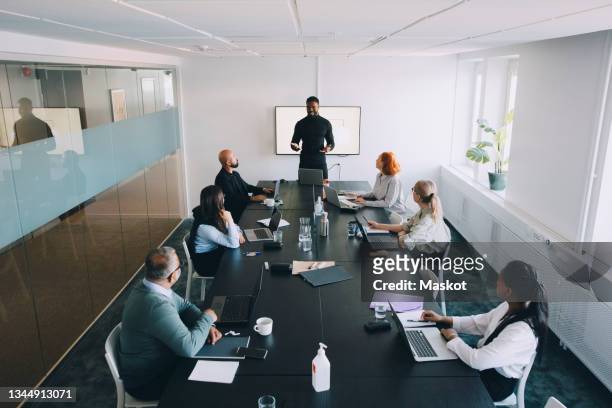 high angle view of businessman giving presentation colleagues in board room at office - board room stock-fotos und bilder