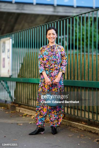 Guest wears a black with multicolored flashy flower pattern oversized long sleeves jumpsuit, a blue shiny leather with gold chain handbag from Stella...