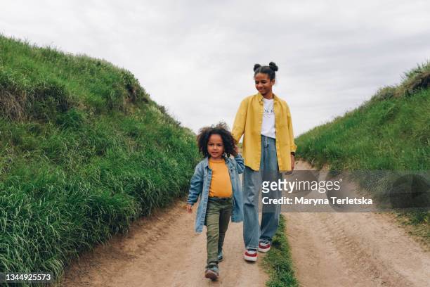 two dark-skinned sisters are walking in nature. - african kids stylish fotografías e imágenes de stock