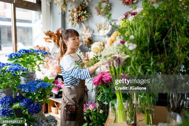 female florist arranging flowers in her shop - japanese flower arrangement stock pictures, royalty-free photos & images