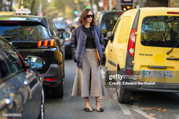 Erika Boldrin wears black sunglasses, a silver chain pendant necklace, a black t-shirt, a navy blue oversized bomber coat, a high waist beige with...